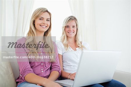 Sisters sitting and smiling on the couch looking at the camera as they hold a laptop