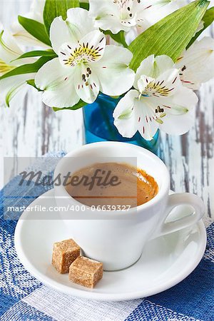 Cup of coffee with brown sugar and white flowers.