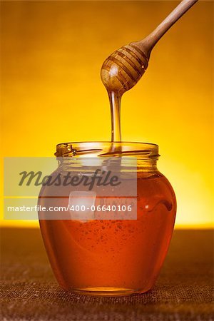 Honey jar with dipper and flowing honey, canvas background