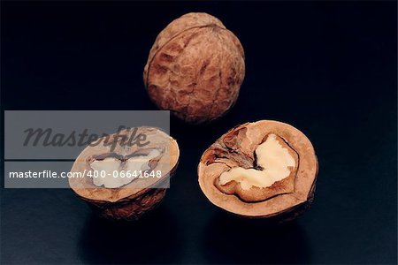 Halves of a walnut and the whole nut are a dark background