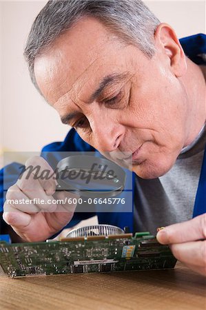 Man Looking at Circuit Board with Magnifying Glass in Studio