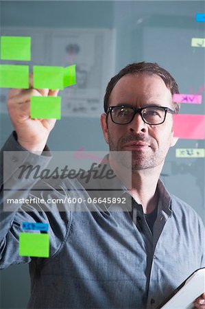 Businessman Looking at Self Adhesive Notes on Glass Board in Studio