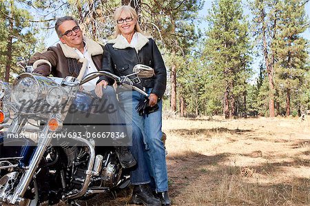Senior couple lean on motorcycle in forest