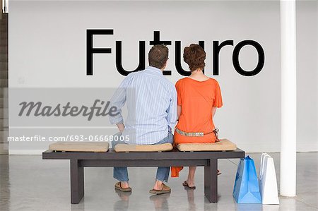 Rear view of couple seated on bench reading Spanish text "Futuro" (future) on wall