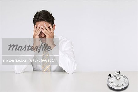 Worried businessman at table with stopwatch representing loss of time