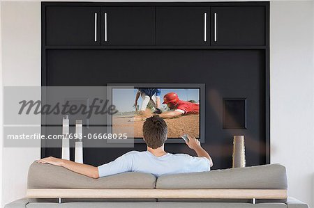 Back view of mid-adult man changing channels with television remote control in living room