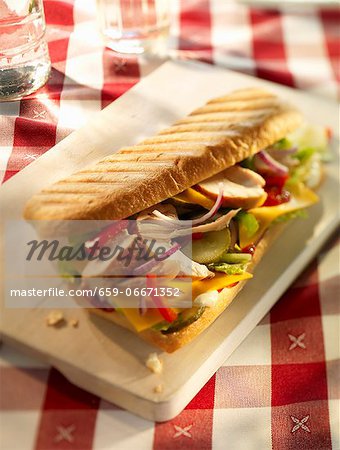 Chicken, onion, pepper, gherkins, cheese slices, lettuce and ketchup in a baguette on a wooden board