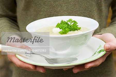 A woman holding a bowl of celery soup with crème fraîche and parsley