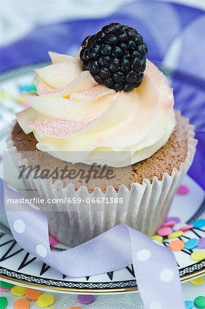 A vanilla cupcake with cream and a fresh blackberry