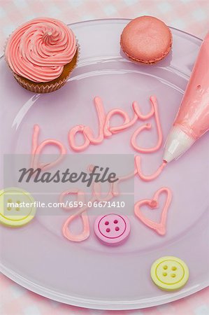 A pink cupcake, macaroons and letters iced with a piping bag for a baby shower