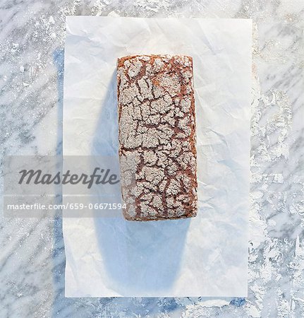 A wholemeal sandwich loaf on paper, on a marble slab, dusted with flour