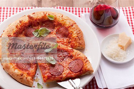 Pizza with salami and basil; one slice of the pizza is on a pizza shovel