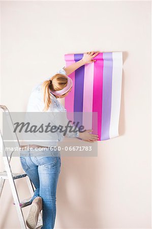 Studio Shot of Young Woman Holding Wallpaper up to Wall