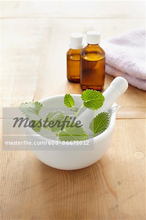 Still life of mortar and pestle with lemon balm, fresh herbs, towel, bottles of essential oil for aromatherapy