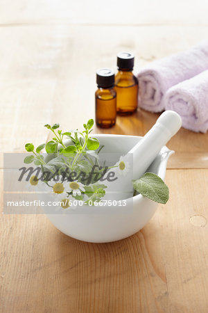 Still life of mortar and pestle with fresh herbs, chamomile, rolled towel, bottles of essential oil for aromatherapy Still life of mortar and pestle with fresh herbs, chamomile, rolled towel, bottles of essential oil for aromatherapy
