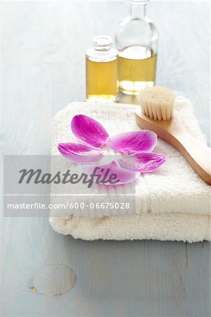 Orchid petals on a towel, brush, bottles of oil, wellness