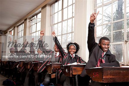 A group of students in a classroom raise their hands to answer a question