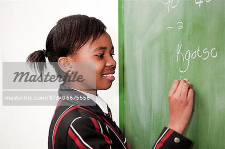View from the side of a smiling female highschool student writing on a chalkboard