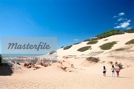 South America, Brazil, Ceara, Morro Branco, tourists with a local guide walk across the dunes past sandstone cliffs at Morro Branco