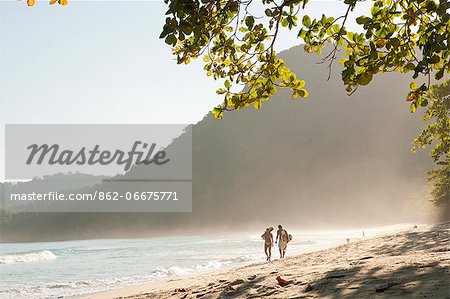 Brazil, Rio de Janeiro State, Costa Verde, Green coast,, Paraty, a couple with a surf board and a guitar walking along Praia do Sono beach near Trindade