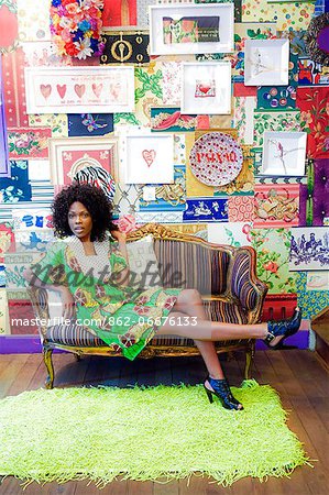 South America, Brazil, Sao Paulo, Jardins, an Afro Brazilian model in designer clothing with a tropical motif sitting on a sofa in the garimpo fuxique boutique in Sao Paulo
