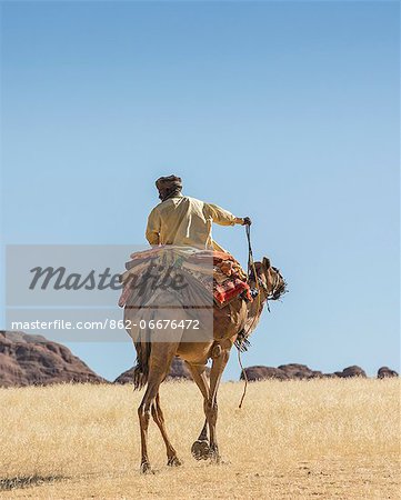 Chad, Bechike, Ennedi, Sahara. A Toubou nomad riding a camel near Bechike.