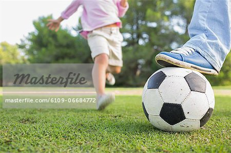 Father holding ball with foot with son running to kick it