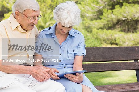 Smiling elderly couple using tablet in the park