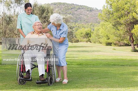 Elderly man in wheelchair chatting with his nurse and partner