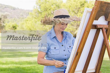 Woman in straw hat painting in the park