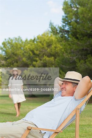 Man in straw hat relaxing in deck chair with his partner approaching