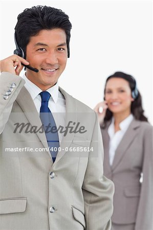 Smiling customer support employee with colleague behind him against a white background