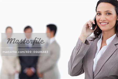Smiling saleswoman on mobile phone with colleagues behind her against a white background