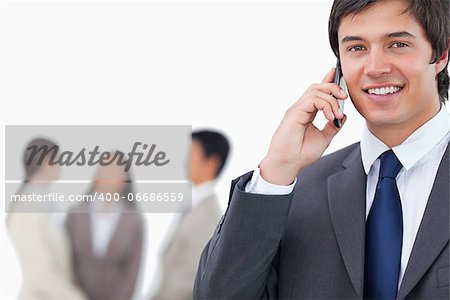 Smiling salesman on his cellphone with team behind him against a white background