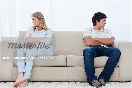 A angry couple sit at the two ends of the couch with their arms folded looking away