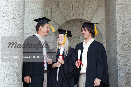 Happy graduates speaking together with university in backgroung