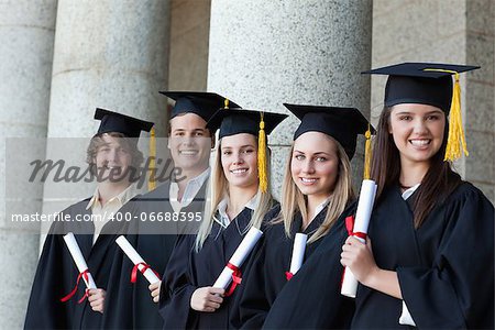 Smiling graduates posing in single line with columns in background