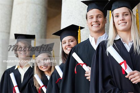 Close-up of five graduates posing in front of the university