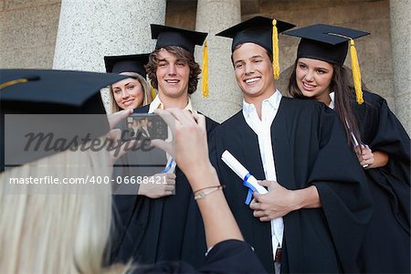 Close-up of a blonde graduate taking a picture of her friend in front of the university