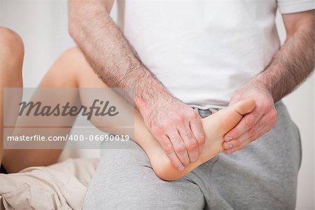 Reflexologist manipulating the foot of his patient while holding it on his thigh indoors