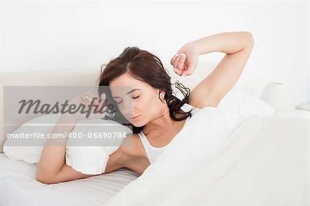 Brunette woman stretching her arms while lying in her bedroom