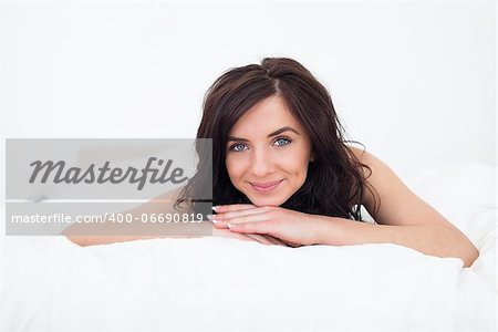 Brunette woman lying on her white duvet in her bedroom