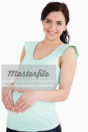 Pregnant woman making a heart with her hands on her belly against white background