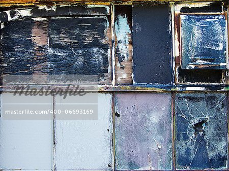 A window on the outside of an old warehouse where the various window panes have been broken and covered up with different fragments of wood forming an unusual texture of urban decay.