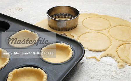 Pastry circles being cut and lining a metal bun tin for jam tarts