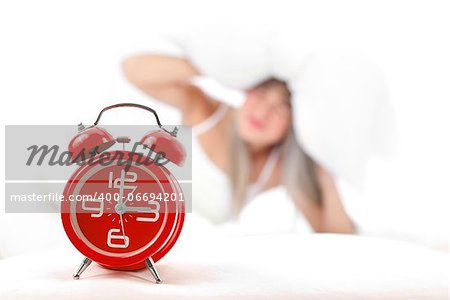 Sleepy woman lying in bed with alarm clock in front