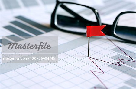 Business concept. Red flag thumbtack near spectacles on paper background with business chart
