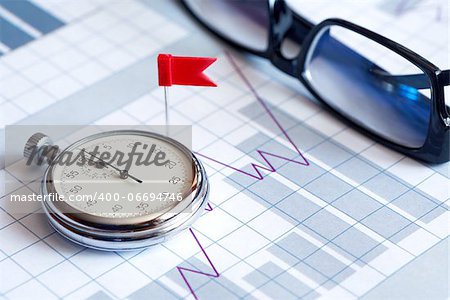 Business concept. Red flag thumbtack near stopwatch and spectacles on paper background with business chart