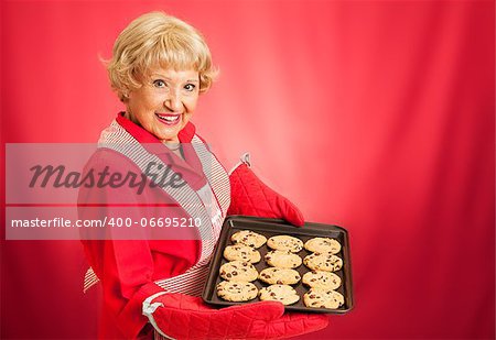 Sweet adorable grandmother holding a pan of freshly baked chocolate chip cookies.   Photographed over red background with room for text.