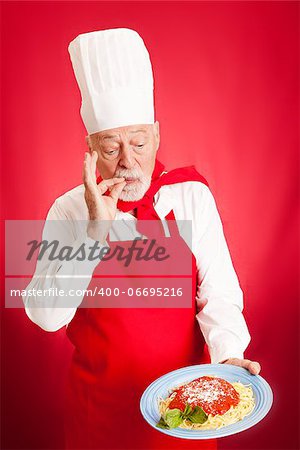 Experienced Italian chef holding a plate of his spaghetti with fresh basil and marinara and kissing his fingers to show how delicious it is.